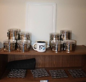 lot 43 image: (2) Silver 4 cannister sets, cutting board, Set of 4 wavy metal trivets, and cups as shown
