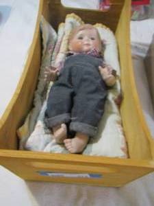 lot 275 image: Porcelain baby boy Doll in wooden crib, comes with hand made blanket- no name
