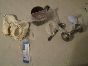 lot 141 image: COLLECTION OF BABY ITEMS  on RIBBON  -   BABY MOCCASINS, CUP , RATTLE, , PACIFIER,  SPOON AND FORK  by  ROGERS SILVER