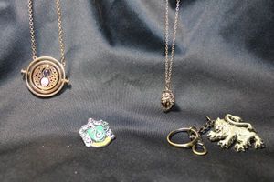 lot 209 image: Harry Potter jewelry selection. Includes Gryffindor keychain, Hermione 18k GP Time Turner articulated hourglass necklace, Slytherin pin, Gryffindor Lion Face necklace