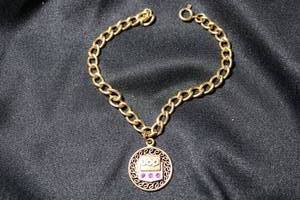 lot 51 image: 12K Gold Filled charm bracelet with UOP logo and 30-year anniversary rubies. Bracelet marked 1-20 12K GF. 7L. Pendant marked 1-20 12K GF on jump ring. Rubies tested.