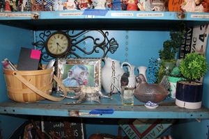 lot 49 image: Home decor artificial plants, pink glass chicken dish, white serving dish set, clock, painted shell, and sewing supplies