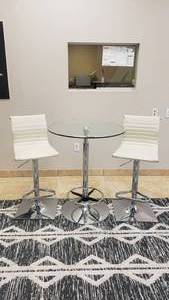 lot 440 image: Beautiful Modern Glass Top Table w Adjustable Foot Rest & 2 White & Stainless Adjustable Barstool Chairs