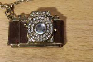 lot 101 image: Leather wrapped and crystal adorned camera pendant on 32L cable chain necklace. Lobster clasp. Camera pendant is 1.75L