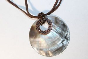 lot 140 image: Signed Carolee bohemian rawhide necklace with Mother of Pearl and hammered bronze metal disc pendant, Marked Carolee on extender hang tag. 14L with 2 extender,