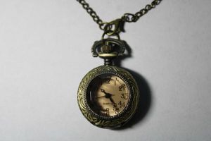 lot 153 image: Pocket watch style watch 32L antiqued chain. Front pink crystal opens like a locket when top pressed. Back decorated with flower design.