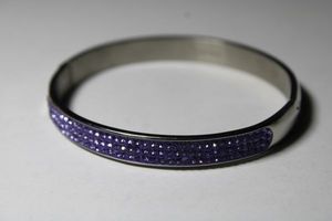 lot 186 image: Signed JCM (Jacmel Jewelry, 2014 - ) Stainless Steel hinged bangle with purple crystals. Marked JCM Stainless Steel inside.