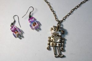 lot 253 image: Novelty Robot jewelry. Fully articulated bronze color 1.5L robot on a 18L necklace. Lobster clasp. Includes a pair of robot ear wire earrings with gumball bodies. 1.5L