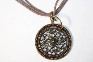 lot 324 image: Signed Coldwater Creek coppered disc pendant on woven leather corded necklace with brass end caps. Has Coldwater Creek hang tag. Lobster clasp. 28L with 2 extender.
