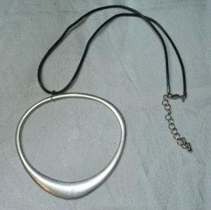 lot 104 image: Signed unusual Fossil brand matte finish elliptical space pendant on corded necklace. 16L with 2 extender. Lobster clasp. Pendant marked Fossil and 3H x 3W