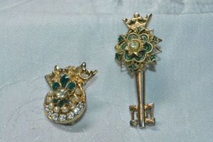 lot 250 image: Signed Coro enamel pin set. Includes key crown 2.25L and round with crown (this one has oxidization and damage to very top). Both marked Coro