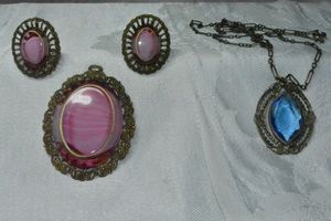 lot 288 image: Filigree border glass jewelry. Includes pink glass pendant and matching clip earrings (Marked W. Germany) and blue glass vintage 22L short and long chain necklace.