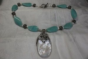 lot 67 image: Signed Merav (Indonesia, QVC) Sterling Silver Mother of Pearl oval disc pendant with foliate frame and Aventurine carved necklace. Marked 925. Toggle clasp. 18L. Overall 22L