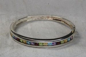 lot 243 image: Sterling Silver multi gemstone faceted channel set gemstone hinged bracelet. Marked 925. Includes Amethyst, Blue Topaz, Citrine, Peridot and Garnet.