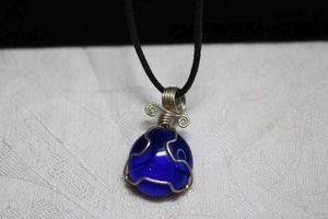 lot 98 image: Artisan crafted wire wrapped deep blue glass pendant on braided leather cord necklace. Hook clasp. 16L