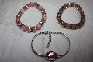 lot 107 image: (3) Pink glass bracelets. Faceted pink glass cabochon silver finish bracelet. Lobster clasp. 6-7L. Faceted pink glass stretch bracelet and pink crackle glass stretch bracelet