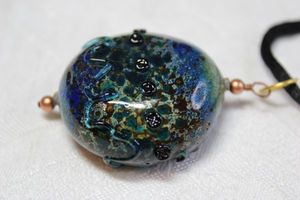 lot 153 image: Dark greentealblue mottled and graduated ombre color with lampwork accents. On black woven 22L cord with adjustment slide bead and lobster clasp. Pendant about 2L