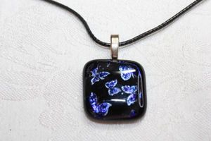 lot 157 image: Dichroic glass pendant with metallic butterflies and black ground. On a woven leather necklace 18L. Pendant 1.5L