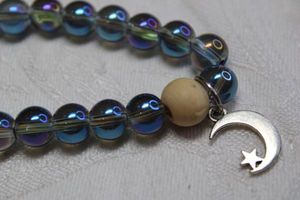 lot 204 image: Blue iridescent glass bead stretch bracelet with single focal wood bead and moon & star charm.
