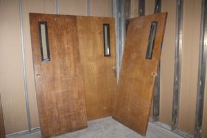 lot 127 image: 3 Solid wood doors. HEAVY All have small window. 2 are 36x80x1-34, 1 is 32x80x1-34. Needs hardware.