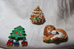 lot 292 image: (3) Holiday broochespins. (2) are marked HMK (Hallmark) on back. Includes Lion and lamb, glitter tree and tree with train dangles.