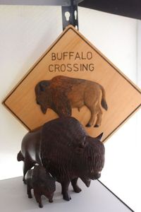 lot 69 image: Two Iron Wood Hand Carved Buffalo with Wood Hand Carved Buffalo Crossing sign