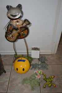 lot 97 image: Frog themed lot - metal frog playing guitar, iron frog door stops, yellow ceramic smiling piggy bank, wooden shelf frog, frog wind chime