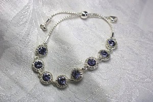 lot 567 image: Bright silver finish Tanzanite glass and rhinestone halo bracelet. Pull adjust.