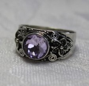 lot 480 image: Silver finish stainless steel ring with faceted Lavender glass bezel set crystal. Decorated on shoulders with flowers, scrolls and beadwork. Size 8.5