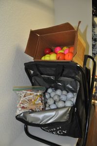 lot 166 image: Fold up golf Stool with pouches. Main compartment full of golf balls, Also Small Box of colored golf balls and large amount of tees