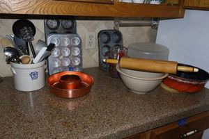 lot 185 image: Baking pans, Copper pan, muffin tins, bread bowl with rolling pin, Pyrex measuring cups, plastic cake holder, and  pottery utensil holder and contents