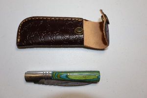 lot 249 image: 2.75 blade Folding pocket knife with leather sheath.  Green and blue wood grain handle.
