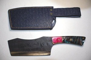lot 265 image: 7 blade cleaver, sunken curved top with textured black top.  Wood and resin handle. Leather sheath.
