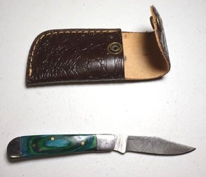 lot 7 image: Pocket knife with leather sheath.  Blue and green wood grain handle.