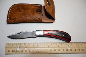 lot 10 image: Pocket knife with leather sheath.  Red and Grey wood grain handle.