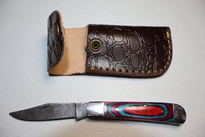 lot 11 image: Pocket knife with leather sheath.  Pink and blue wood grain handle.