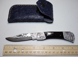 lot 12 image: Pocket knife with black resin handle. Leather sheath.