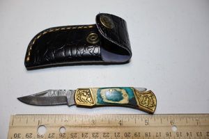 lot 17 image: Folding Pocket knife with green and natural wood grain handle. Leather sheath.