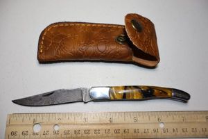 lot 18 image: Folding Pocket knife with gold and black resin handle. Leather sheath.