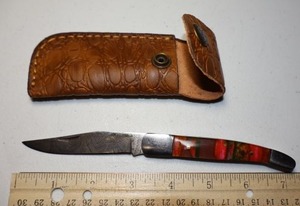 lot 23 image: Folding Pocket knife with leather sheath. Pink and green resin handle.