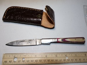lot 28 image: Folding Pocket knife with leather sheath.  Pink and natural wood grain handle.