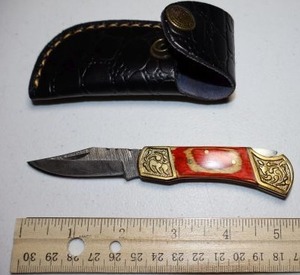 lot 31 image: Folding Pocket knife with leather sheath.  Red and natural wood grain handle.
