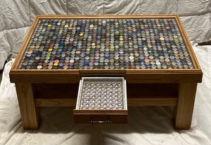 lot 196 image: COFFEE TABLE WITH A SIDE DRAWER WITHBEER CAPS UNDER A GLASS TOP. IN GREAT CONDITION. 18T x 39W