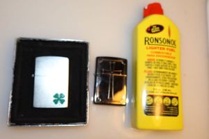 lot 132 image: Zippo Shamrock lighter, Zippo cross lighter, and lighter fuel