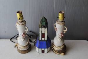 lot 205 image: collectible set consisting of two white porcelain table lamps with floral details and a central stained glass lamp shaped like a lighthouse.  See all pictures