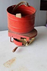 lot 443 image: vintage Cyclone seed spreader featuring a metal bucket and a wooden base with a hand crank.