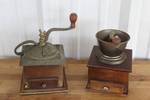 Two vintage manual coffee grinder  featuring a wooden box base and one has a decorative cast iron top mechanism.