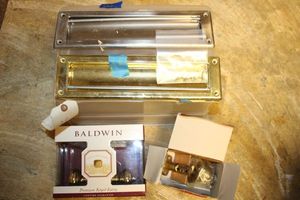 lot 139 image: Household items unopened Baldwin keyed entry knob, mail slots, and Kwikset lock