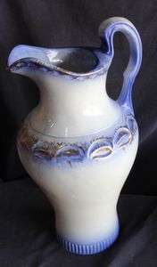 lot 27 image: La Belle Flow Blue China Water Pitcher with a rounded body, a gracefully curved handle, and a floral pattern in cobalt blue.