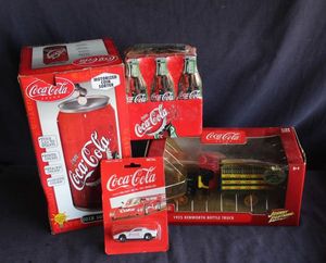 lot 114 image: Collection of Coca-Cola collectibles featuring a boxed 1935 Kenworth Bottle Truck Model. A Motorized coin sorter shaped like a soda can. Blister-packed Miniature die-cast vehicle.
